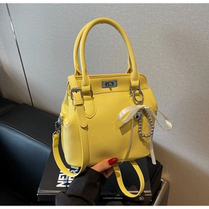 Detail of yellow lychee leather handbag featuring silver twist lock and ribbon charm