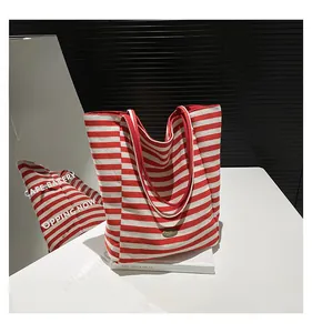 Detail of red and white striped canvas tote bag featuring an oval bronze metal logo plate