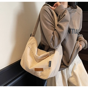 Detail of beige canvas crossbody tote showing brown leather logo and large moon shape