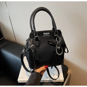 Detail of black lychee grain tote bag with silver twist lock and ribbon heart charm