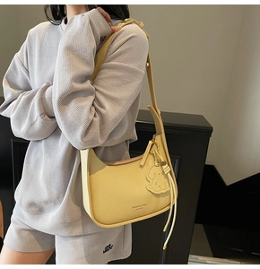 Detail of yellow litchi leather crescent underarm bag with dog charm and fashion bag logo