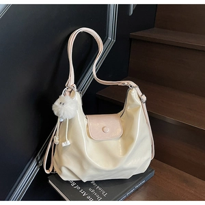 Détail d'un sac cabas brillant beige et rose avec pompon doux sur un escalier chic