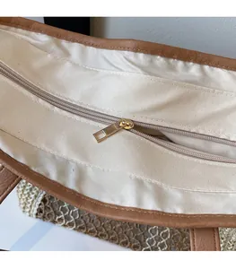 Detail view of woven straw bag featuring gold metal zipper and brown leather trim edging