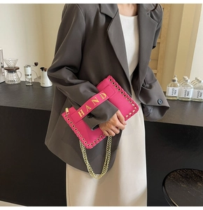 Detailed macro view of pink woven envelope bag with gold rivets and HAND letter embroidery