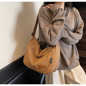 Detail view of brown canvas tote showing leather brand tag and functional metal zipper