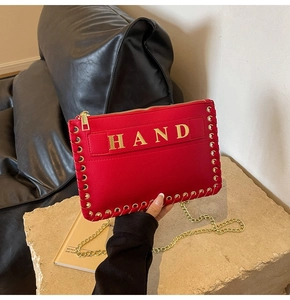 Detail of red leather envelope bag with gold 'HAND' lettering and woven metal chain strap