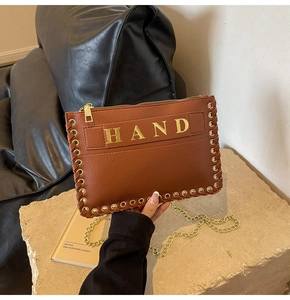 Detail of brown leather envelope bag with gold HAND metal lettering and woven rope edges