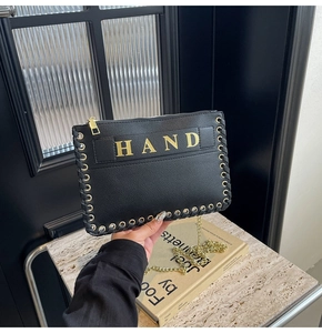 Detail showing woven metal eyelets and gold HAND lettering on black envelope bag