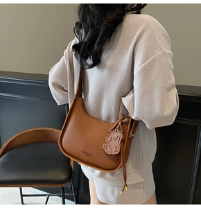 Rear view of brown lychee texture hobo bag with fashion bag text and puppy charm on model