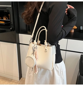 Close-up of white lychee pattern leather bucket bag with knotted handle and tassel detail