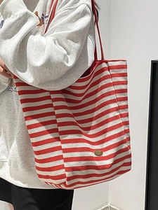Striped canvas tote bag in red and white with vintage plaque, shown on shoulder