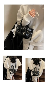 Detail of black pleated bucket bag with shiny finish and lace bow pearl charm
