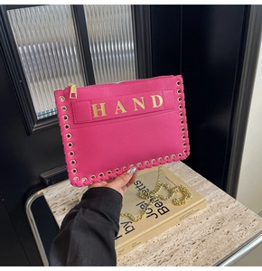 Detail of fuchsia litchi pattern envelope bag with gold HAND lettering and woven chain