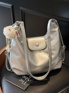 Sac fourre-tout argenté minimaliste avec breloque en peluche sur un fauteuil en cuir