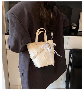 Gros plan d'un sac seau en cuir ciré beige avec nœud en dentelle sur blazer gris