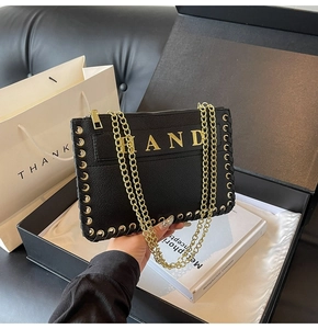 Detail of black pebbled leather handbag with gold HAND text and metal eyelet weave