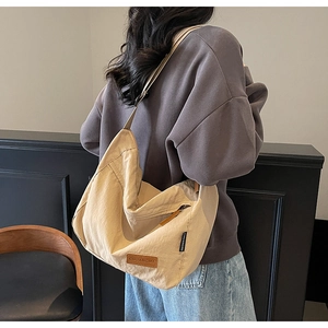 Detail view of large beige canvas tote bag with brown brand leather patch and shoulder strap