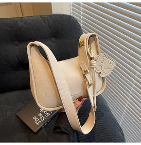Detail of off-white lychee grain hobo bag with gold hardware and bear charm on sofa