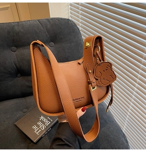 Detail of lychee textured brown leather hobo bag with a dog-shaped charm on a sofa