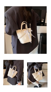 Détail du sac seau crème avec nœud en dentelle, pendentif et bandoulière en chaîne