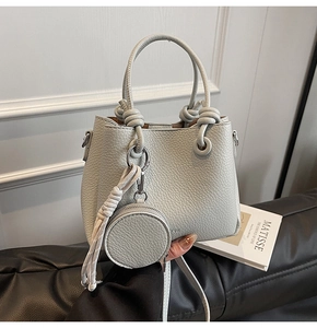 Detail of grey pebbled leather bucket bag with knot handle and round coin purse charm
