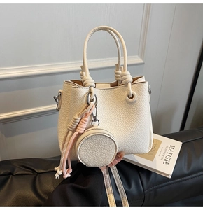 Close-up of beige lychee grain bucket bag with wave edge and round coin purse charm
