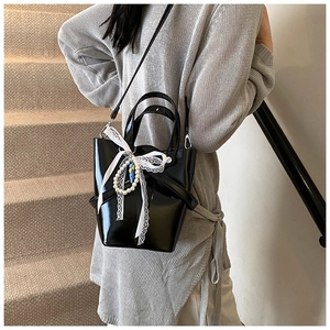 Détail du sac seau noir en cuir ciré avec nœud en dentelle et breloque en perles à l'épaule