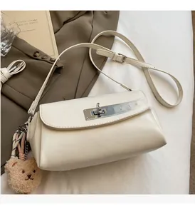 Detail of creamy white leather handbag with silver metal turn lock and bear charm