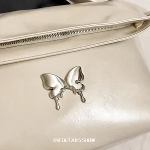 Détail macro du papillon en métal argenté sur un sac fourre-tout en cuir crème doux