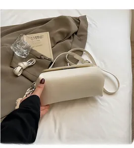 Detail of cream leather shoulder bag with plush ball charm and ribbon on bed