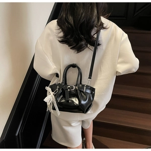 Detail of black glossy pleated bucket bag with pearl lace pendant on wooden stairs
