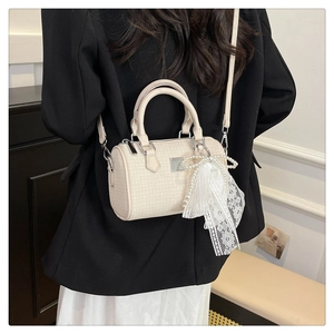 Detailed view of beige tweed Boston bag with pearl bow charm worn on a black blazer