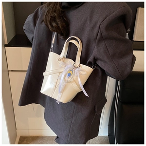 Détail du sac seau blanc cassé avec nœud en dentelle et charm bleu sur veste