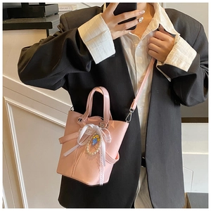Détail du sac seau rose en cuir ciré avec nœud en dentelle et pendentif en perles