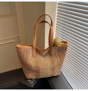 Detail of hollow-out straw woven tote bag with brown leather handles on black sofa
