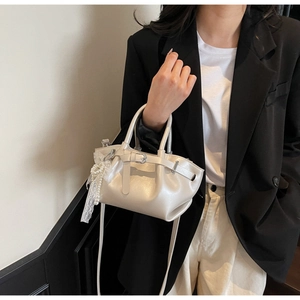 Detail view of cream white pleated bucket bag with pearl lace charm and shoulder strap