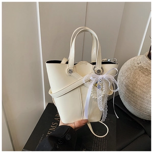 Détail du sac seau crème avec design croisé en cuir et accessoire en dentelle élégant