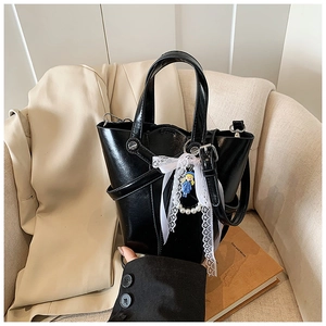 Détail du sac seau en cuir verni noir avec un nœud en dentelle et un pendentif perle