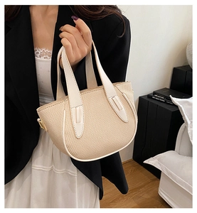 Detail of beige woven tote bag with white leather handles and gold metal buckles