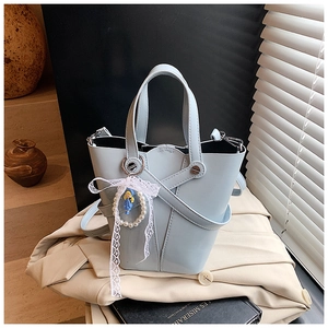 Détail du sac seau bleu clair avec sangles croisées et breloque en perles et dentelle