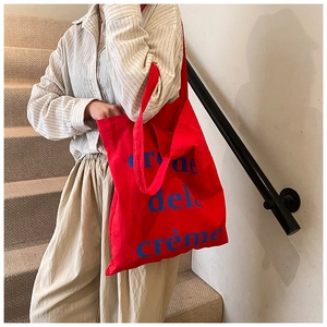 Détail du sac cabas en toile rouge avec texte bleu sur une tenue rayée décontractée