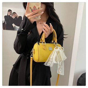 Detail of yellow woven Boston bag featuring a white lace bow and pearl charm accessory