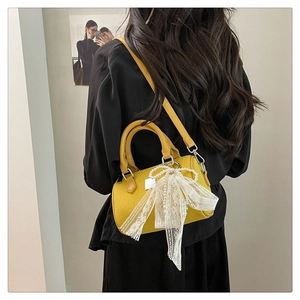 Detail of yellow boston bag with woven texture and white lace bow accessory
