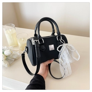Close-up of black textured Boston bag featuring a silver metal plate and pearl bow charm
