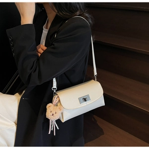 Detail of cream flap crossbody bag with silver rotating lock and cute bear charm