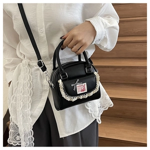 Detail of black faux leather Boston bag with white lace trim and plaid bow decoration