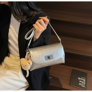 Detail of silver metallic pillow bag with turn-lock clasp and cute plush bear charm