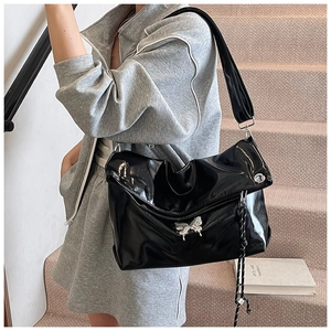 Détail d'un grand sac cabas en cuir verni noir avec boucle papillon argentée et zip en corde