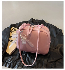 Detailed view of pink glossy underarm bag with double zippers and pearl lace bow charm