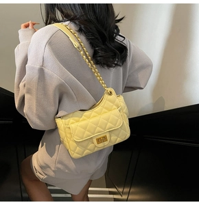 Detail of yellow quilted underarm bag featuring a metallic turn-lock and chain strap